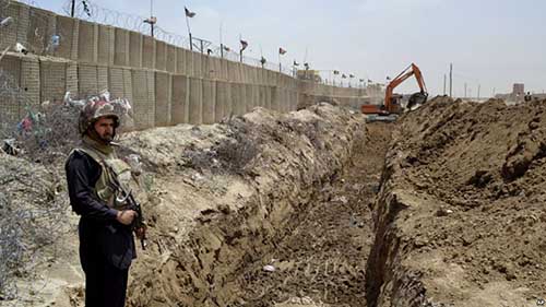 FILE - In this May, 16, 2014 file photo, a Pakistani border guard stands alert as an excavator digs a trench along Pakistan Afghanistan border at Chaman post in Pakistan.