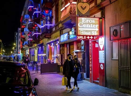 A couple wearing face masks walk through the red light district in Frankfurt, Germany, Saturday, March 14, 2020. For most people, the new coronavirus causes only mild or moderate symptoms, such as fever and cough. For some, especially older adults and people with existing health problems, it can cause more severe illness, including pneumonia.(AP Photo/Michael Probst)