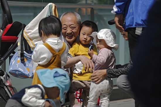 An elderly man plays with children near a commercial office building in Beijing on May 10, 2021. China's ruling Communist Party will ease birth limits to allow all couples to have three children instead of two to cope with the rapid rise in the average age of its population, a state news agency said Monday, May 31. (AP Photo/Andy Wong)